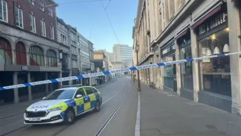 Police tape across an empty city centre street with a police car parked behind the cordon