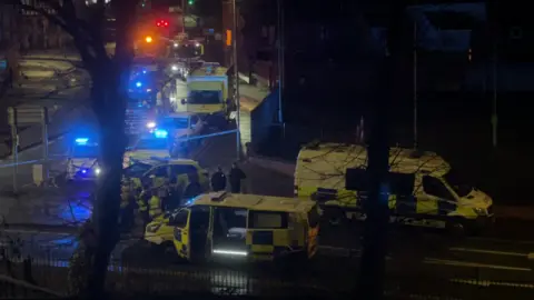 Police vans and a occurrence  motor  seen done  the trees connected  a thoroughfare  by Chester station, with bluish  lights flashing and officers gathered connected  the road.