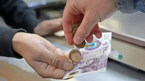 A hand putting a twenty pound note and coins into another hand.