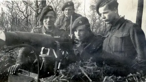 John Arthur John aiming a machine gun with three other soldiers next to him