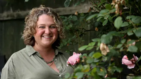 Gloucestershire Hospitals NHS Trust Cancer patient Anoushka Duroe-Richards smiles standing in a flower garden.