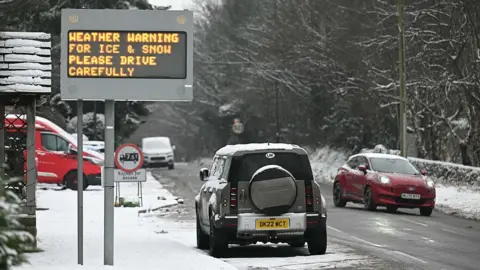 Getty Images Motorists pass a sign cautioning drivers to drive carefully in the snowy conditions in the town of Glossop, Derbyshire, on 6 January 2026. 
