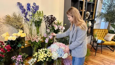 Alla Orekhovska touching some flowers in her new shop. There are a dozen displays of different flower types, including roses, which she is adjusting.