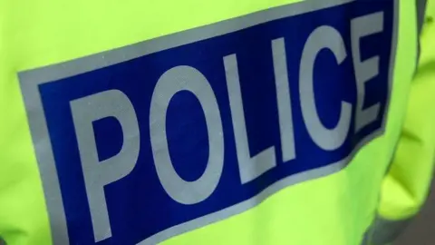 The back of a police officer's high visibility jacket. The word "police" is in silver letters on a blue background.
