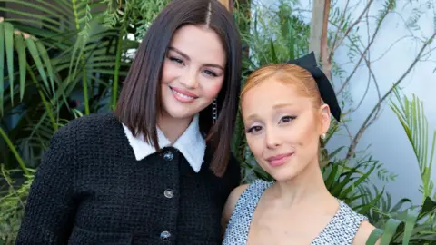 Shutterstock Selena Gomez and Ariana Grande at the Academy Women's Luncheon Presented in Los Angeles in December. Gomez is wearing a black boucle jacket with a white collar, while Grande is wearing a black and white sleeveless dress.