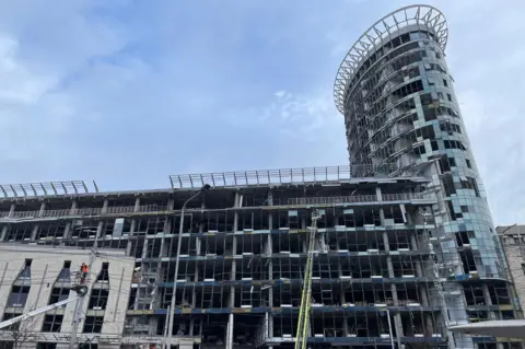 The damage caused to the Kyiv business center. A crane can be seen inspecting the building, whose windows have been blown out.