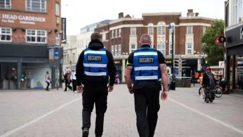Charnwood Borough Council The backs of two street security staff wearing blue and black uniforms 