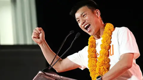 People's Party leader and prime ministerial candidate Natthaphong Ruengpanyawut, wearing a white T-shirt with an orange garland around his neck, addresses a campaign rally ahead of the general election in Bangkok on January 25, 2026