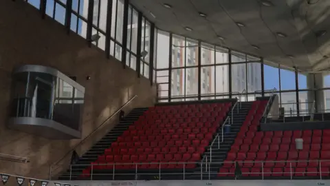Aaron Law Rows of red seats in a stand with large glass windows behind them
