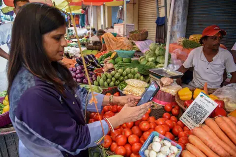NurPhoto via Getty Images A woman uses her phone to scan a QR code of the digital payment app Paytm after purchasing some vegetables at a market in Kolkata, India, on August 4, 2025. 
