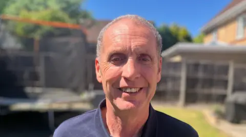 John Hatton stood in a garden with a trampoline in the background