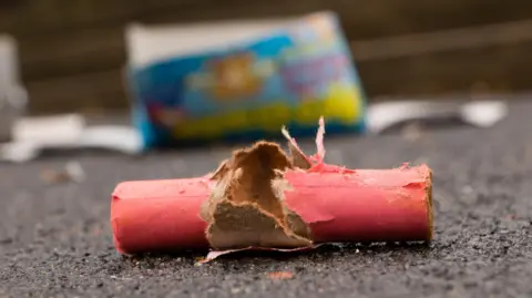 Waste of burnt firecrackers on the street. The packaging is red. Other remains of fireworks can be seen lying about.