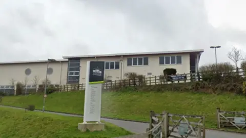 A cream coloured college building with a footpath beside an a sign reading Truro College.