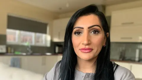 BBC Sharanjeet in a grey jacket, sat in a kitchen