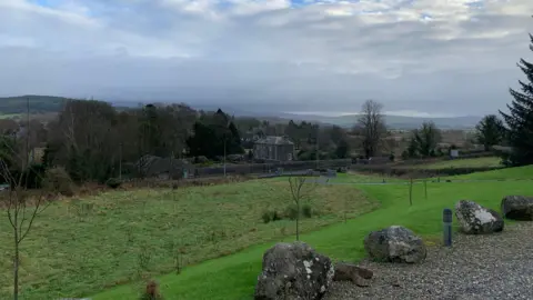 A view across the south of Scotland countryside with a house sitting among trees and green rolling hills