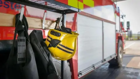 A yellow firefighter's helmet hanging on the side of a red fire engine