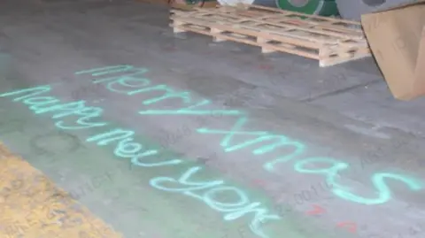 WMP The words are written in green on the grey, concrete floor of a warehouse