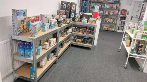 Brick Shack Metal shelves covered in Lego sets in a white room with grey carpet.