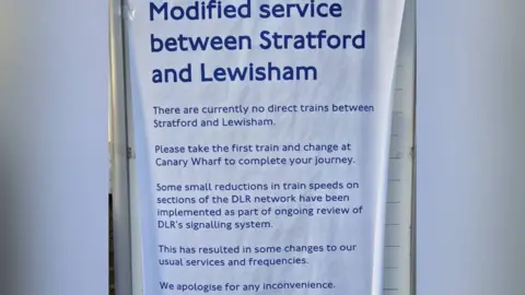 Poster which says: Modified Service between Stratford and Lewisham.
There are currently no direct trains between Stratford and Lewisham. Please take the first train and change at Canary Wharf to complete your journey. Some small reductions in train speeds on sections of the DLR network have been implemented as part of ongoing review of DLR's signalling system. This has resulted in some changes to our usual services and frequencies. We apologise for any inconvenience.