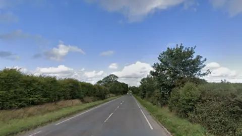A long bypass road which is surrounded on both sides by green grass and hedges. There is a green tree on the right hand side