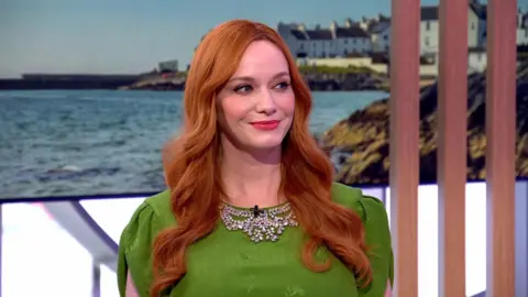 Christina Hendricks smiles. She wears a green dress and has long, wavy red hair.