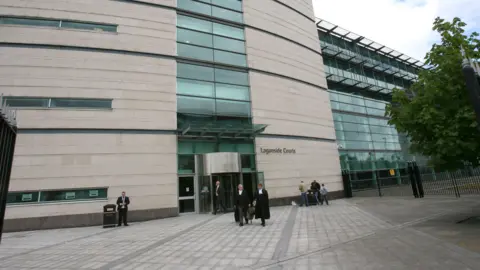 PA Media Men in suits walk out of Belfast Magistrates' Court. The court is a cream building with panes of glass. 