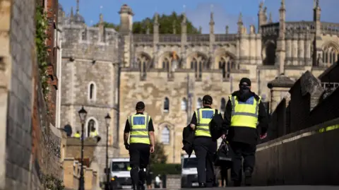 Getty Images Three police officers wearing hi-viz vests are pictured walking from behind. They are walking in the direction of Windsor Castle, which is visible in the background. 