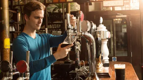 A man wearing a blue top pouring a pint in a pub