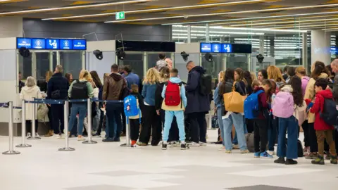 Travellers with luggage queue at arrivals as officials in booths marked "all passports" check passports at Split Airport in Croatia.