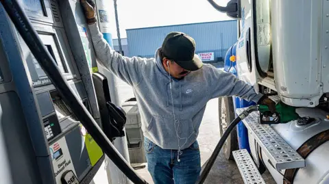 A driver refuels a tractor trailer with diesel fuel while keeping an eye on the nozzle at a Chevron truck stop