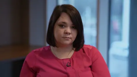 A woman with a brown bob, wearing a dark pink top