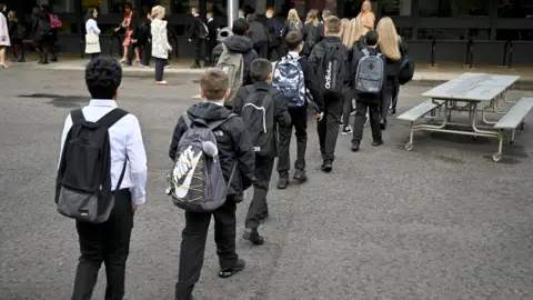 Getty Images A line of school children carrying bags walking across a playground.
