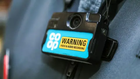 Co-op A body-camera on a Co-op staff member. The camera has a Co-op logo and a warning sign to show that people are being 'audio & video' recorded.