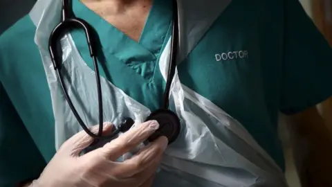 A doctor in green scrubs holding a stethoscope.