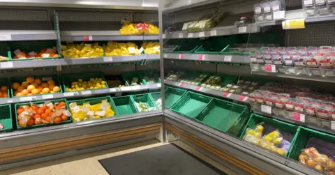 A picture of the fruit shelves at Waitrose on the Rohais in Guernsey. In the image are large bags of oranges, lemons alongsidxe boxes of grapes and some blueberries. They're all organised into green crates.