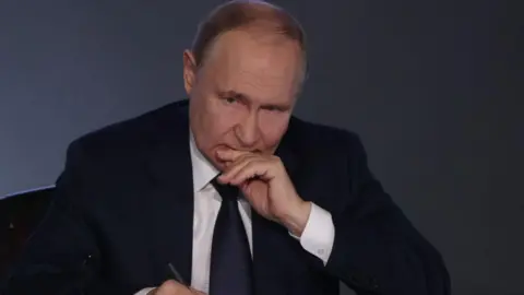 Getty Images Vladimir Putin resting his head on his hand and holding a pen