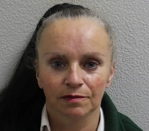 Metropolitan Police Custody image of Tina Smith, wearing a dark jacket and white shirt, photographed against a plain wall.