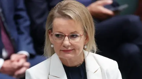 Sussan Ley looks off camera in a white jacket