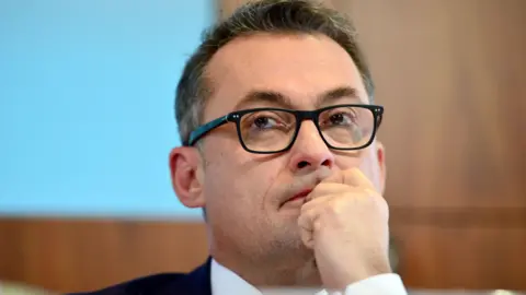 Getty Images Joachim Nagel wearing glasses and holding his hand to his mouth pensively