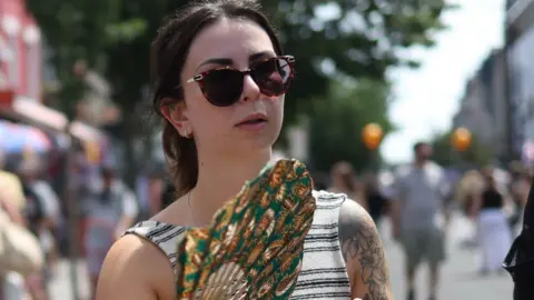Woman in stripy top and sunglasses carrying a fan