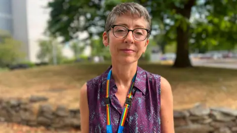 Chief medical officer Vanessa Purday has short grey hair. She is wearing a purple top with a rainbow lanyard.