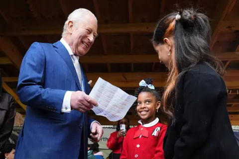 Pool via Getty Images The King laughs while holding a sheet of paper in his hand while meeting a woman and child at the Harlem Grown community initiative in Upper Manhattan on Wednesday.
