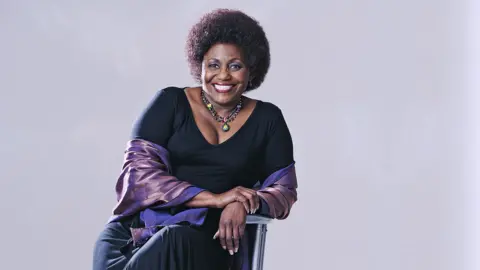 Media 24 / Gallo Images is a photo of a photo displayed by actress Nandi Nimp, who pretends to be the camera while smiling and sitting on a chair in a studio for photography against a gray background, taken in South Africa in 2007.