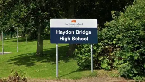 A school sign on grass stating 'Haydon Bridge High School' with 'Northumberland County Council' written above it. 