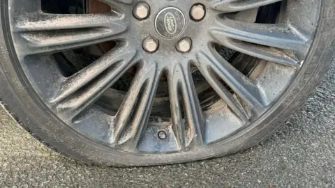 A black car wheel with a central Land Rover photographed close up. The tyre is has been burst and is flat.