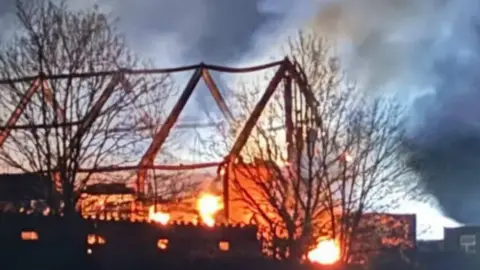 Louis Lovelock Outline of barn building on fire - the outline of the roof timbers can be seen and the sky is filled with large amounts of smoke.
