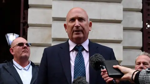 Getty Images Radd Seiger, in a navy suit and blue tie, addresses the media outside a court building.