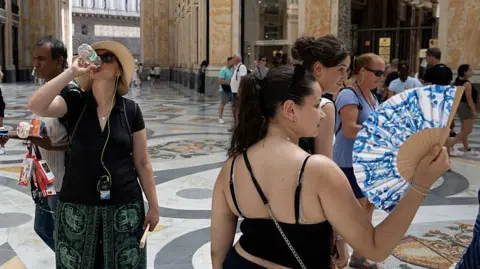 Anadolu via Getty Images People drink water and use hand fans to protect themselves from the sun in Naples, southern Italy. Photo: 1 August 2026