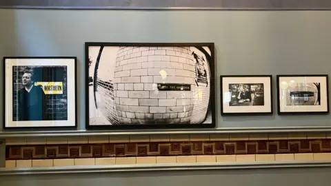 Photograph taken from inside the exhibition of framed photos from the collection hung on a gallery wall.