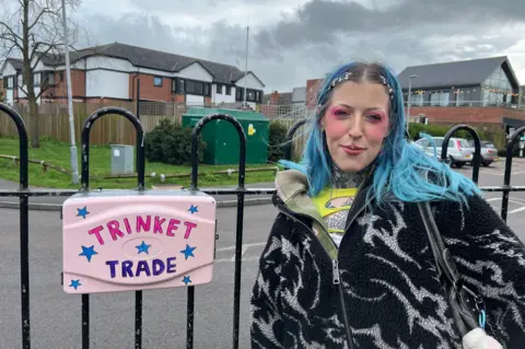 BBC Ashleigh Pithers standing outside her trinket trade box in Nottingham, before it was stolen. The box is pink and blue and she had blue hair. She's wearing a black and white fleece.